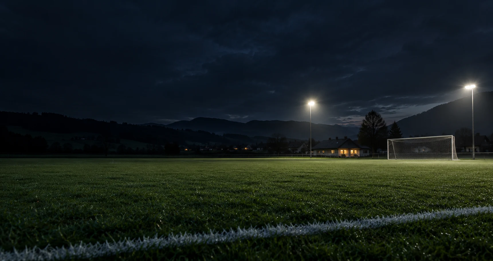 Ein Amateurfußballplatz im Flutlicht vor österreichischen Hügeln